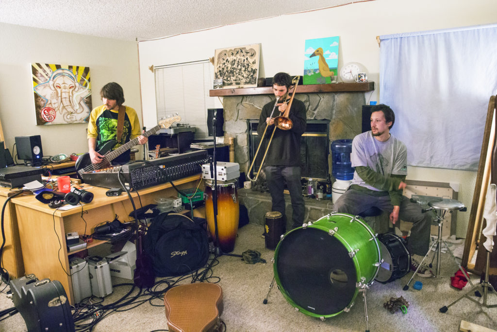 Local Santa Cruz band, Boostive, practices in their makeshift living room studio. Bandmates Brian McNamara (bass), Nathan Kocivar (trombone, right and saxophone, left) and Seiji Komo (drums) begin their practice session by switching instruments with each other and freestyling their set. Photo by Casey Amaral